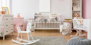 Cameretta di una neonata, ben organizzata con culla e giocattoli, tutti bianchi e rosa.