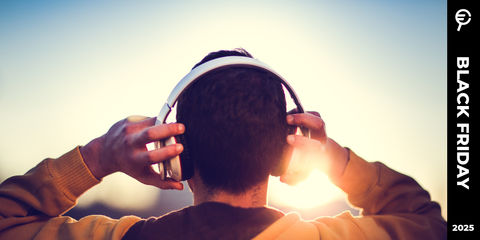 Persona di spalle con cuffie bianche sulle orecchie, illuminata dal sole al tramonto che crea un’atmosfera calda. Sulla destra scritta promozionale per Black Friday