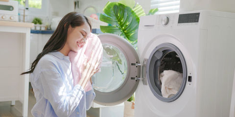 Donna tiene tra le mani un panno appena uscito dall'asciugatrice appoggiandolo al viso