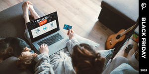 Persona seduta sul divano con laptop aperto su offerte Black Friday, carta di credito in mano e cane accanto