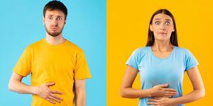 Uomo e donna con espressione di disagio tengono una mano sull’addome, su sfondo colorato, a rappresentare problemi digestivi.