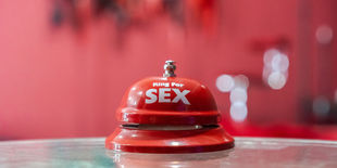 Campanello da tavolo di colore rosso con scritta bianca ben visibile, posizionato su superficie lucida con sfondo sfocato nelle stesse tonalità.