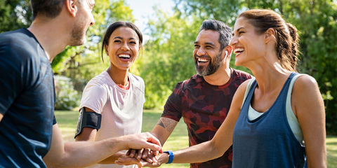 Quattro persone sorridenti in abbigliamento sportivo uniscono le mani all’aperto in un parco, dopo attività fisica insieme