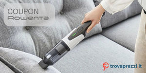 Mano che utilizza un aspirapolvere portatile per rimuovere polvere e briciole dalla superficie di un divano grigio con logo di Trovaprezzi.it in basso a destra