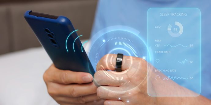 migliori smart ring Persona tiene in mano uno smartphone blu e indossa uno smart ring nero con grafica digitale che mostra dati sul sonno.
