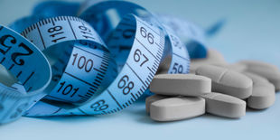 Metro da sarta avvolto accanto a compresse bianche su superficie azzurra, simbolo di dieta, controllo del peso e integrazione alimentare