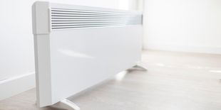 Termoconvettore bianco moderno appoggiato a terra su pavimento chiaro, posizionato accanto a una parete bianca.