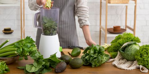 Persona che prepara un frullato verde inserendo lime in un frullatore con spinaci e avocado.