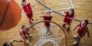 Bambine in divisa rossa osservano il pallone da basket che sta per entrare nel canestro durante una partita in palestra.