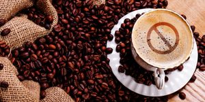 Tazza di caffè con simbolo di divieto sulla superficie, circondata da chicchi di caffè e sacchi di juta.