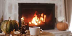 tazza bianca e zucca autunnale in primo piano con sfondo di un camino acceso