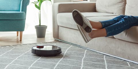 robot aspirapolvere su tappeto grigio con gambe di donna sollevate