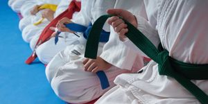 Judoka seduti sul tatami con cinture colorate tra le mani in posizione di rispetto.