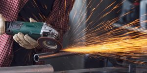 Lavoratore taglia un tubo metallico con smerigliatrice, generando numerose scintille arancioni.