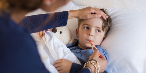Bambino a letto con termometro in bocca, assistito da un adulto che gli tocca la fronte.