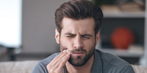 Uomo che si tocca la guancia con espressione dolorante come per mal di denti.