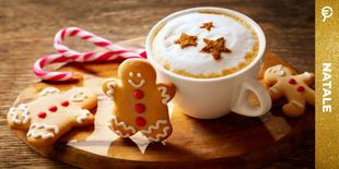 Cappuccino decorato e biscotti natalizi gingerbread su tagliere in legno, proposta per idee regalo prima colazione.