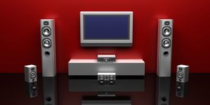 Sistema audio da salotto composto da torre di casse, subwoofer centrale e soundbar, in ambiente moderno con sfondo rosso.