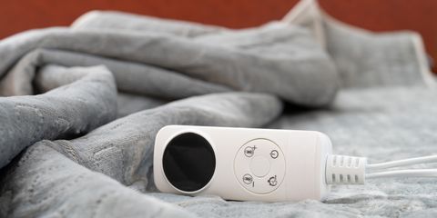 Telecomando bianco per coperta elettrica appoggiato su tessuto grigio morbido, avvolto in pieghe soffici.