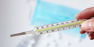 Termometro al mercurio tenuto in mano, con scala graduata visibile e sfondo sanitario sfocato