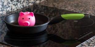 Padella su superficie a induzione lucida con salvadanaio rosa all’interno, immagine simbolica legata a risparmio energetico e consumi.