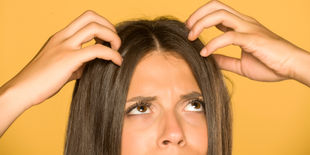Donna con espressione preoccupata che si gratta la testa con entrambe le mani su sfondo giallo uniforme.