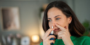 Una donna utilizza uno spray nasale, concentrata nell'applicazione per alleviare il fastidio nasale.