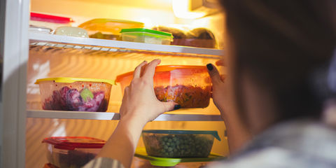 Donna che appoggia nel frigorifero un contenitore con del cibo all'interno, vicino ad altri contenitori di cibo.