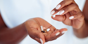 Mano aperta con capsule e compresse di vari colori mentre l’altra mano ne prende una, su sfondo chiaro e neutro