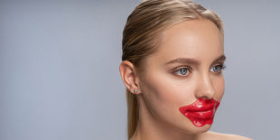 Donna con capelli raccolti e sguardo laterale indossa una maschera labbra rossa, evidenziando effetto volumizzante e nutriente.